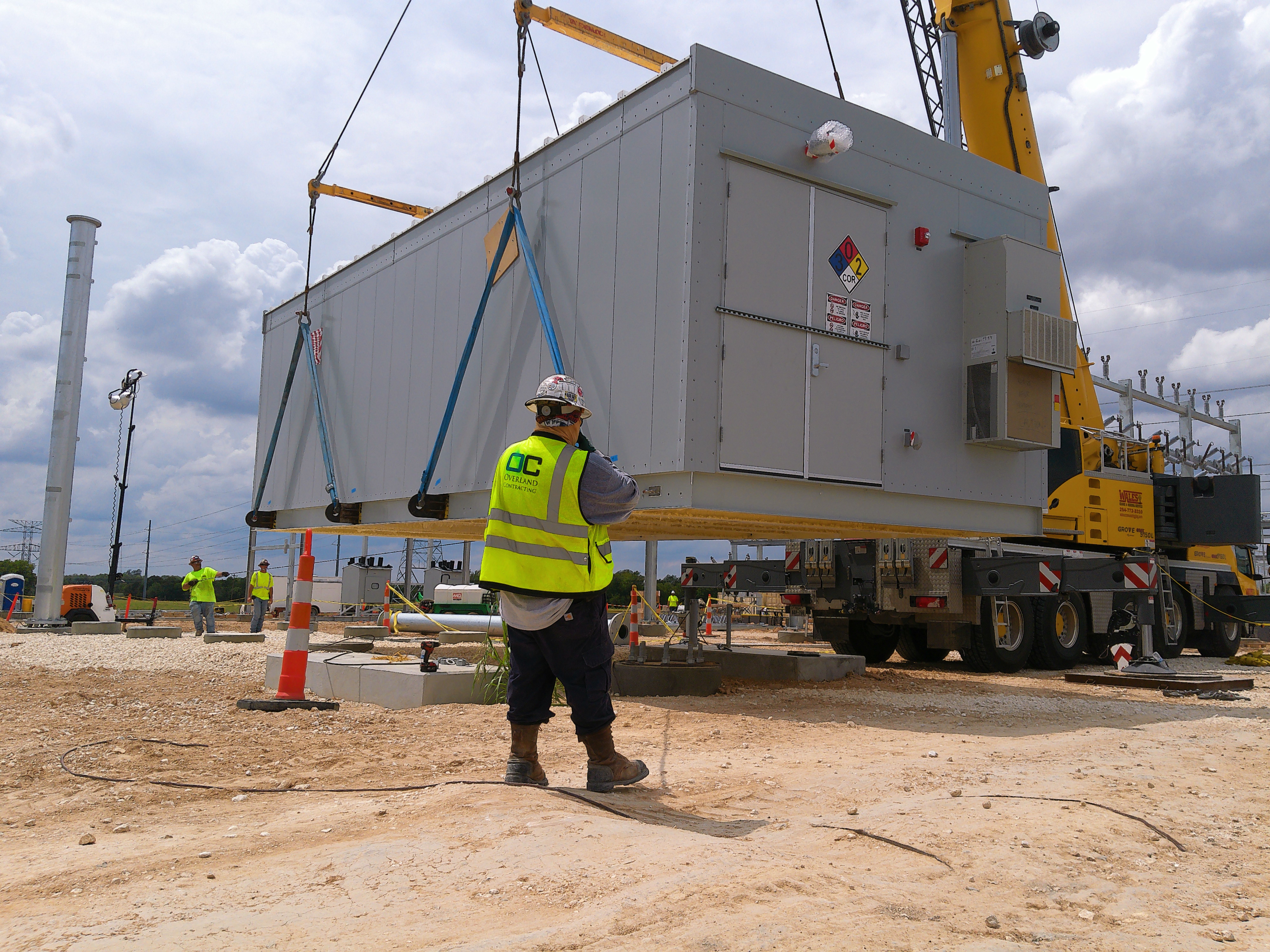 Crown employee in a high-visibility vest and hard hat with an enclosure being lowered by a crane
